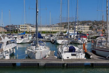 Port Deauville-Trouville limanına yanaşan yelkenli gemiler, güneş ışığına karşı yükselen direkler, sakin ve varlıklı sahil deneyimlerini taşıyan yelkenli gemiler.