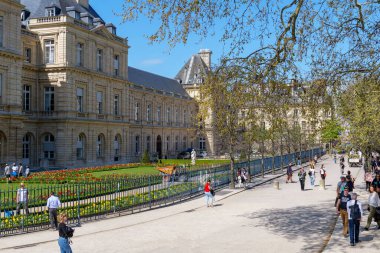 Paris, Fransa - 4 Nisan 2025. Lüksemburg Bahçeleri 'nde bahar günü, canlı çiçekler, yeşil ağaçlar ve zarif saray cephesiyle, insanlar geniş yolda yürürken sakin Paris atmosferinin tadını çıkarıyorlar.