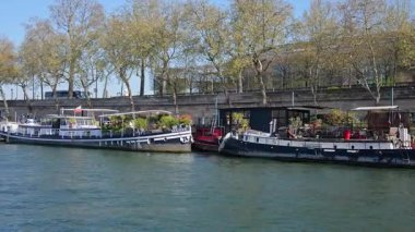 Paris, Fransa - 30 Mart 2025 Tekneler ve yüzen restoranlar Seine nehir seti boyunca. Ağaçlı, sakin sulu ve kentsel seyahat tarzlı Paris manzarası