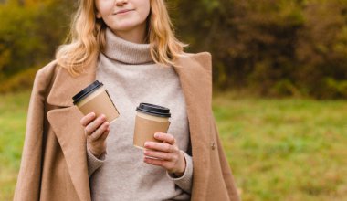 Kadının elinde iki tane kağıt kahve fincanı var. Paket veya teslimat konsepti. Uzayı kopyala Sonbahar yaşam tarzı. Kupa üzerine metin veya logo için yer