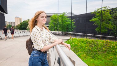 Şehrin arka planında poz veren güzel genç bir kadın. Kız güneşli bir günde rahatlar. Seyahat ve aktif yaşam konsepti.