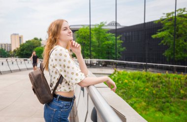 Şehrin arka planında poz veren güzel genç bir kadın. Kız güneşli bir günde rahatlar. Seyahat ve aktif yaşam konsepti.