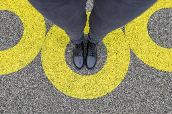 Black shoes standing in yellow circle on the asphalt concrete floor. Comfort zone or frame concept. Feet standing inside comfort zone