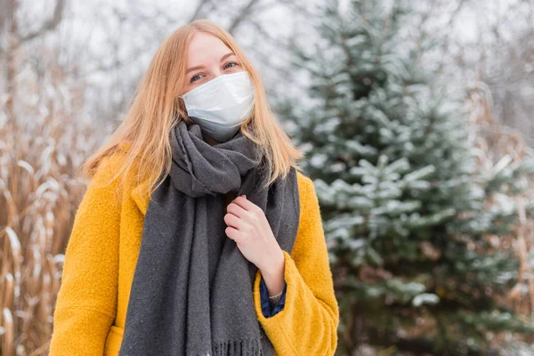 Junge blonde Frau mit weißer medizinischer Gesichtsmaske vor Naturhintergrund, trendy Farben des Jahres 2021 - leuchtend gelb und ultimativ grau. COVID-19 Coronavirus-Pandemie — Stockfoto