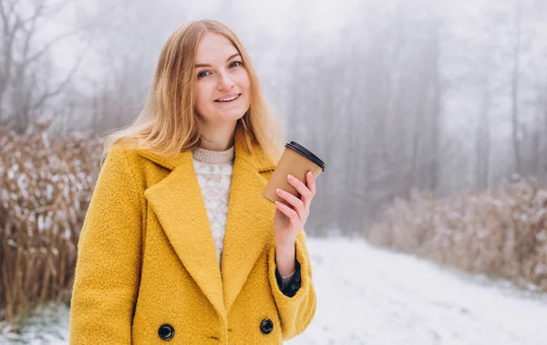Šťastná mladá žena drží papírový šálek kávy nad přírodou pozadí, módní barva roku 2021 - osvětlující žlutá. Odnést nebo doručit koncept. Kopírovat prostor. — Stock fotografie
