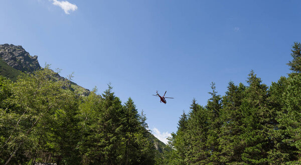 Red helicopter is flying between mountains peak