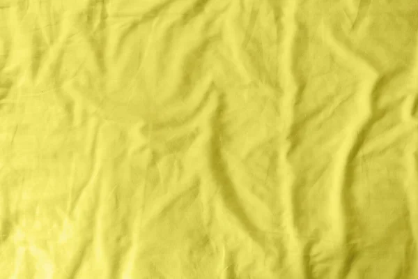 Abstract pattern of a yellow crumpled bed sheet in a hotel room. The manufacturing of bedsheet uses cotton, linen, silk modal and bamboo rayon. Trendy color of year 2021