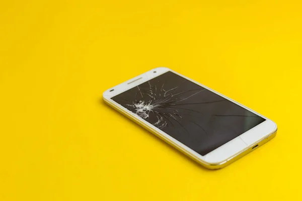 Modern touch screen smartphone with broken screen on yellow background. Flat lay style. Top view. Place for text.