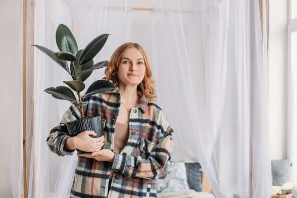 Genç bir kadın taşındıktan sonra neşe içinde yeni bir dairede saksı tutuyor. Güzel genç kız yeni evine yeşil ot getiriyor. Konsept kirala ya da al