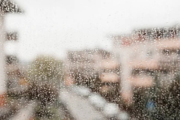 El fondo borroso con las gotas bokeh de la lluvia sobre el cristal de ventana, la ciudad grande. Gotas de lluvia en vidrio de ventana —  Fotos de Stock