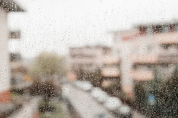 Gotas de lluvia en un cristal de ventana con las formas borrosas de los edificios, la gran ciudad. Gotas de lluvia en vidrio de ventana. Enfoque selectivo. —  Fotos de Stock