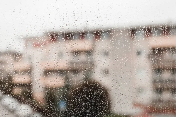 Gotas de lluvia en un cristal de ventana con las formas borrosas de los edificios, la gran ciudad. Gotas de lluvia en vidrio de ventana. Enfoque selectivo. —  Fotos de Stock