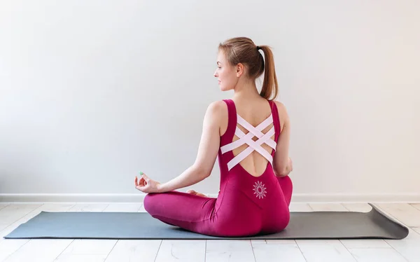 Young healthy beautiful woman practicing yoga at home sitting in lotus pose on yoga mat meditating relaxed. Indoor and outdoor workout. Sport and healthy active lifestyle concept. — Stock Photo, Image