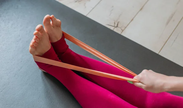 Evde direniş bandı egzersizi. Kadın pilates egzersizi yapıyor. Kapalı alandaki yoga minderinde omuz çalışması için elastik kayışla kollarını çekiyor. Spor ve sağlıklı aktif yaşam tarzı konsepti.