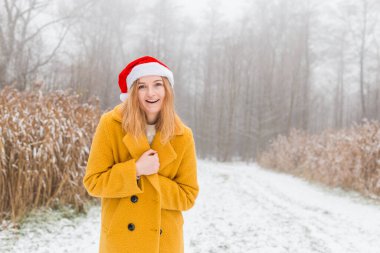 Sarı bir ceket giyen mutlu genç bir kadın, kırmızı şapkalı, doğa arka planında gülümseyen, 2021 yılının moda rengi - aydınlatıcı sarı ve nihai gri, kış zamanı