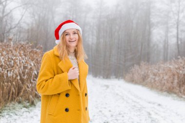 Sarı bir ceket giyen mutlu genç bir kadın, kırmızı şapkalı, doğa arka planında gülümseyen, 2021 yılının moda rengi - aydınlatıcı sarı ve nihai gri, kış zamanı