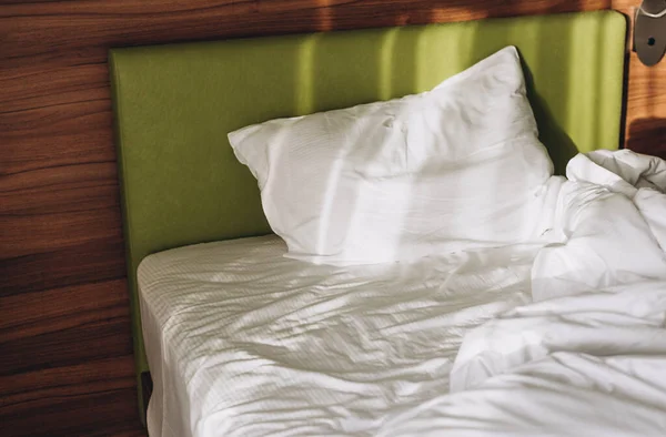 Em uma cama no quarto os raios do sol caem. Cama confortável com roupa de cama branca em casa — Fotografia de Stock