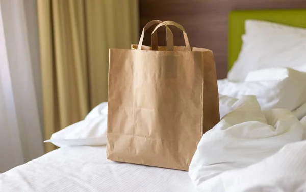 Delivery food craft bag on the bed on sunny day. Delivery in any weather around the clock to the client. Fast food eco packaging with big breakfast set