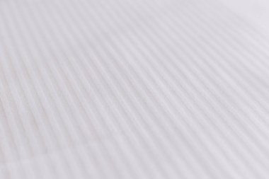 Yatakta zarif tekstil. Kar beyazı çarşafta çizgili desen.