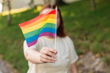 LGBT gökkuşağı bayraklı güzel kırmızı lezbiyen kadın gün batımında yeşil doğa arka planında. Aynı cinsiyet çiftleri için mutluluk, özgürlük ve aşk kavramı.