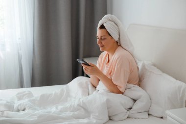 Kafkasyalı mutlu bir kadın evinde rahat bir yatakta rahat rahat mesajlaşarak akıllı telefonuna mesaj atıyor, gülümseyen bir kız cep telefonu kullanıyor, cihaz üzerinde kablosuz interneti tarıyor. Evden online alışveriş kavramı