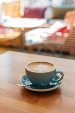 Latte sanatıyla birlikte bir bardak kapuçino. Kafedeki ahşap masada mavi bardakta kahve.