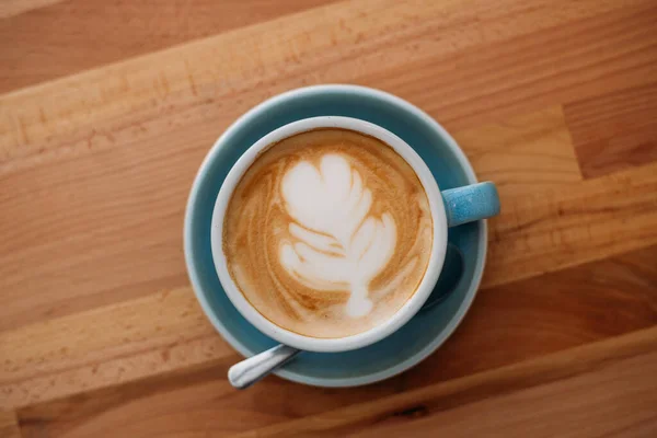 ラテアートとカプチーノのカップ カフェの木のテーブルの上の青いカップのコーヒー — ストック写真