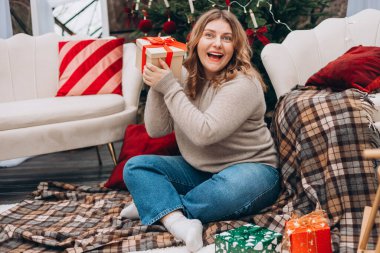 Mutlu Noeller, mutlu bayramlar. Mutlu, genç bir bayan Noel hediyeleri alıyor ve kanepenin yanında yere oturuyor ve Noel ağacını süslüyor..