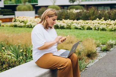 Mutlu 30 sarışın kadın bankta oturuyor ve laptopla çalışıyor, hızlı bağlantı. Dizüstü bilgisayarı olan güzel bir kız sokakta oturuyor. Serbest çalışan biri. Uzaktan çalış.