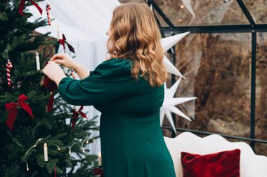 Yeşil elbiseli genç bir kadın evde Noel ağacı süslüyor ve gülümsüyor. Kış ve tatiller. Kutlama bayrağı.