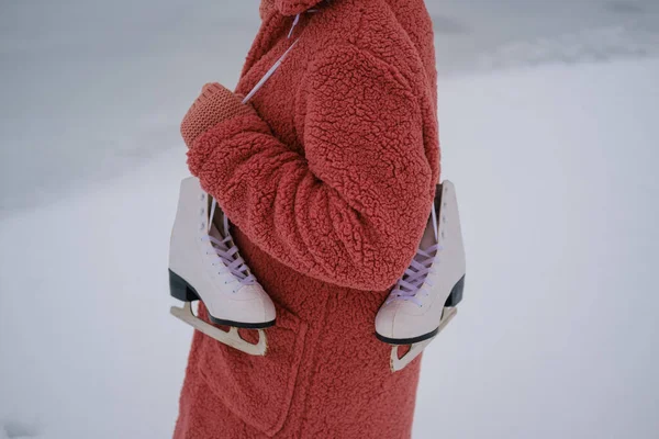ピンクのエコファーのコートを着た若い女性が肩に白いスケートをしています 顔のない体の一部 冬のアイススケートのコンセプト ストック画像