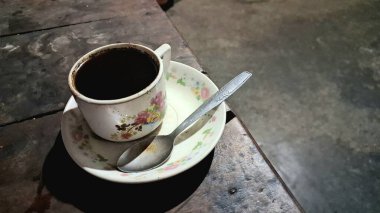 Çiçekli bir fincanda, kırsal ahşap bir masada, tepeden manzaralı koyu bir kahve..