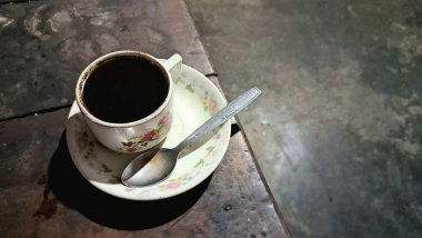 Çiçekli bir fincanda, kırsal ahşap bir masada, tepeden manzaralı koyu bir kahve..