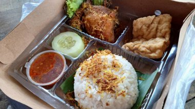 Nasi Kotak olarak bilinen geleneksel Endonezya usulü kızarmış tavuk pirinç kutusu Baharatlı Sambal Tofu ve Taze Sebzeler Yüksek Açı Görünüm Yemek Teslimatı ve Ticari Menüler için Gerçekçi Yemek Fotoğrafı.
