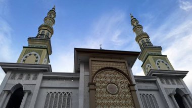 Haşmetli İslami cami mimarisi iki yüksek minareyi ve açık mavi gökyüzü arkaplanına karşı karmaşık geometrik cepheli desenleri barındırır.