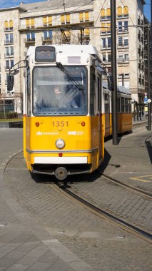 Budapeşte, Macaristan 08-03-2025. Açık sarı Budapeşte tramvayı işlek bir şehir bölgesinde virajlı bir yolda ilerliyor. Şehir hayatı ve tarihi halk trason sistemi, ikonik manzaralı rota.