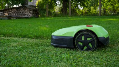 Robotik çim biçme makinesi yeni biçilmiş ve biçilmemiş alanlar arasında açık bir kontrastla sınır teli boyunca çim biçiyor. Akıllı ev teknolojisi, peyzaj, açık hava bakımı ve ev geliştirme.