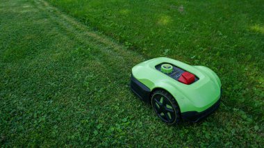 Robotik çim biçme makinesi yeni biçilmiş ve biçilmemiş alanlar arasında açık bir kontrastla sınır teli boyunca çim biçiyor. Akıllı ev teknolojisi, peyzaj, açık hava bakımı ve ev geliştirme.