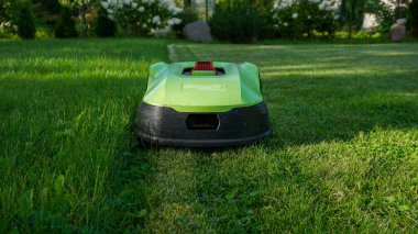 Robotik çim biçme makinesi yeni biçilmiş ve biçilmemiş alanlar arasında açık bir kontrastla sınır teli boyunca çim biçiyor. Akıllı ev teknolojisi, peyzaj, açık hava bakımı ve ev geliştirme.