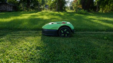 Robotik çim biçme makinesi yeni biçilmiş ve biçilmemiş alanlar arasında açık bir kontrastla sınır teli boyunca çim biçiyor. Akıllı ev teknolojisi, peyzaj, açık hava bakımı ve ev geliştirme.