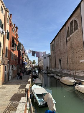 Venedik, İtalya - 11 Ekim 2025: Venedik 'te dar bir kanal yukarıda asılı renkli binalar ve çamaşırhaneler, İtalyan kentsel hayatının özünü yansıtıyor