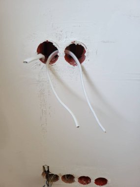 Elektrik kablolarının duvar açıklıklarından çıktığı, kurulum sürecini ve duvar dokusunu vurguladığı, yenilenme atmosferi yarattığı görülüyor.