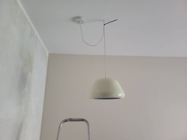 Minimalist bir alanda tavandan sarkan kolye lambası, yumuşak aydınlatma ve parlak tasarım, modern ev estetiği ve iç mimari için ideal.