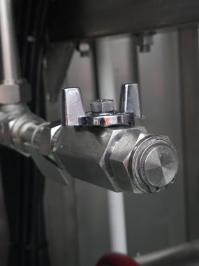 Bir boruya bağlı metalik bir kapakçığa yakın plan, parlak yüzeyi ve endüstriyel tasarımı görünür arka plan detaylarıyla mekanik bir ortamda vurguluyor.