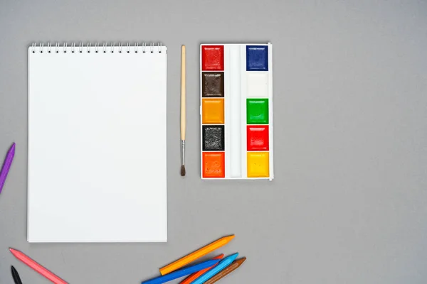 A notepad whith chalks and paints on a gray background — Stock Photo, Image