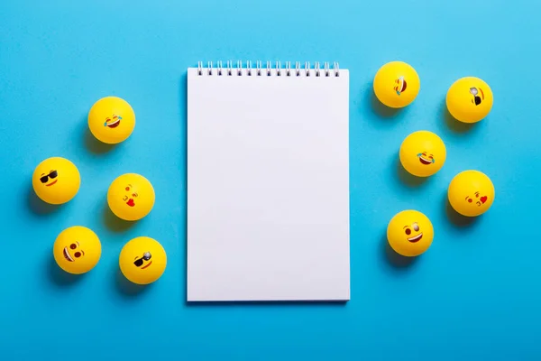 Mavi arka planda farklı emojileri olan birkaç sarı top ve not defteri.