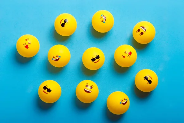 Mavi arka planda farklı emojileri olan birkaç sarı top.