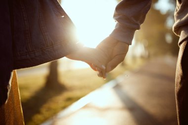 Bir erkek ve bir kız güneşin arka planında el ele tutuşuyorlar.