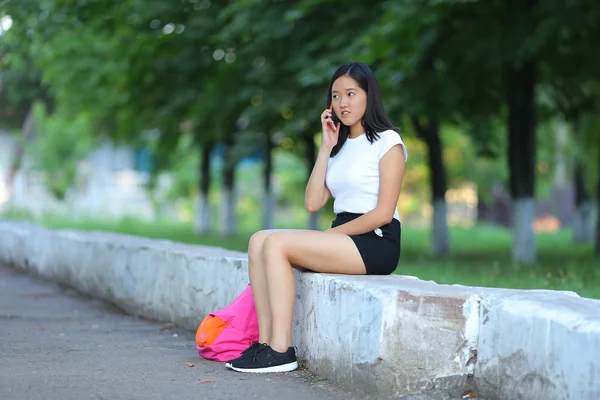 年轻的女孩坐在和谈在公园里电话 — 图库照片