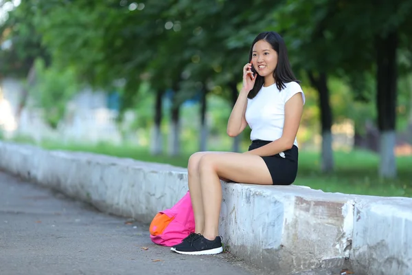 年轻的女孩坐在和谈在公园里电话 — 图库照片